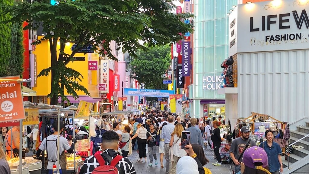Crowded Myeongdong shopping street in Seoul with tourists walking among street food stalls and fashion shops