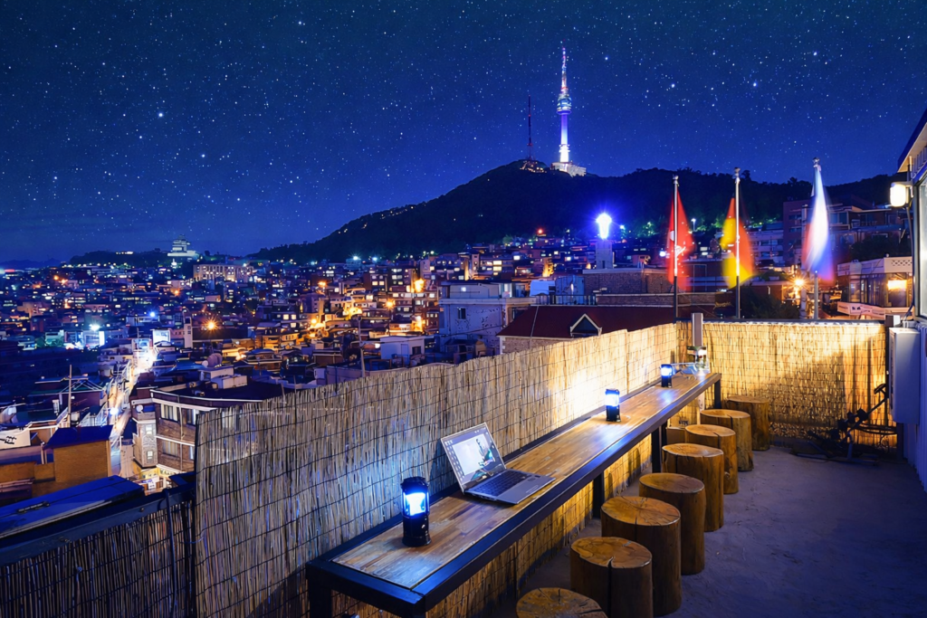 Rooftop seating area at a Seoul guesthouse with a night city view and N Seoul Tower in the background