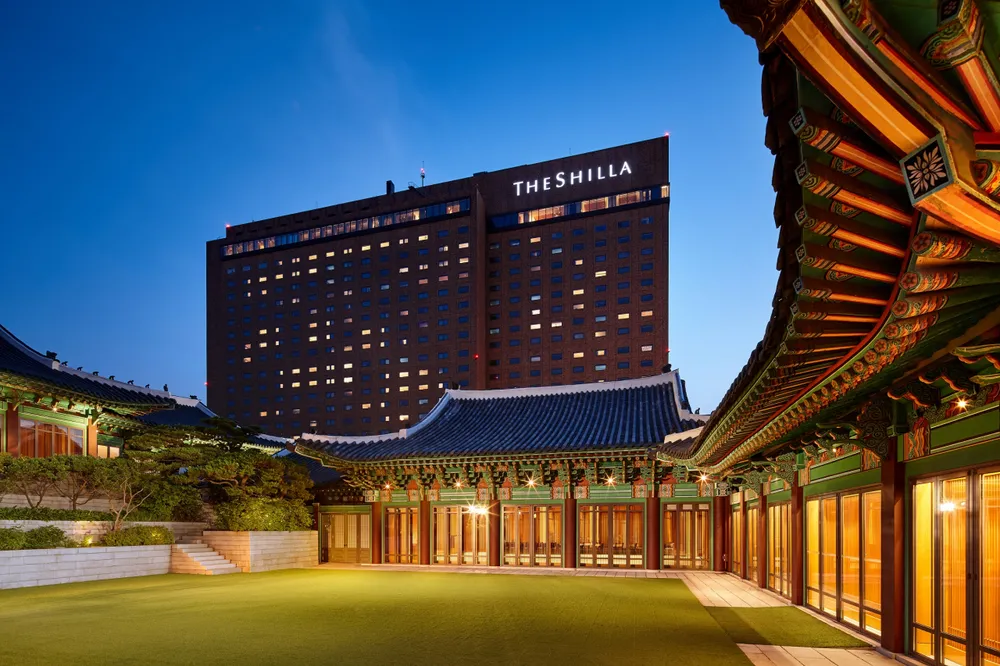 Traditional Korean hanok courtyard with The Shilla Seoul hotel building in the background at dusk