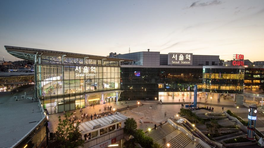 Exterior view of Seoul Station at dusk with illuminated station signage and surrounding plaza in Seoul, South Korea.