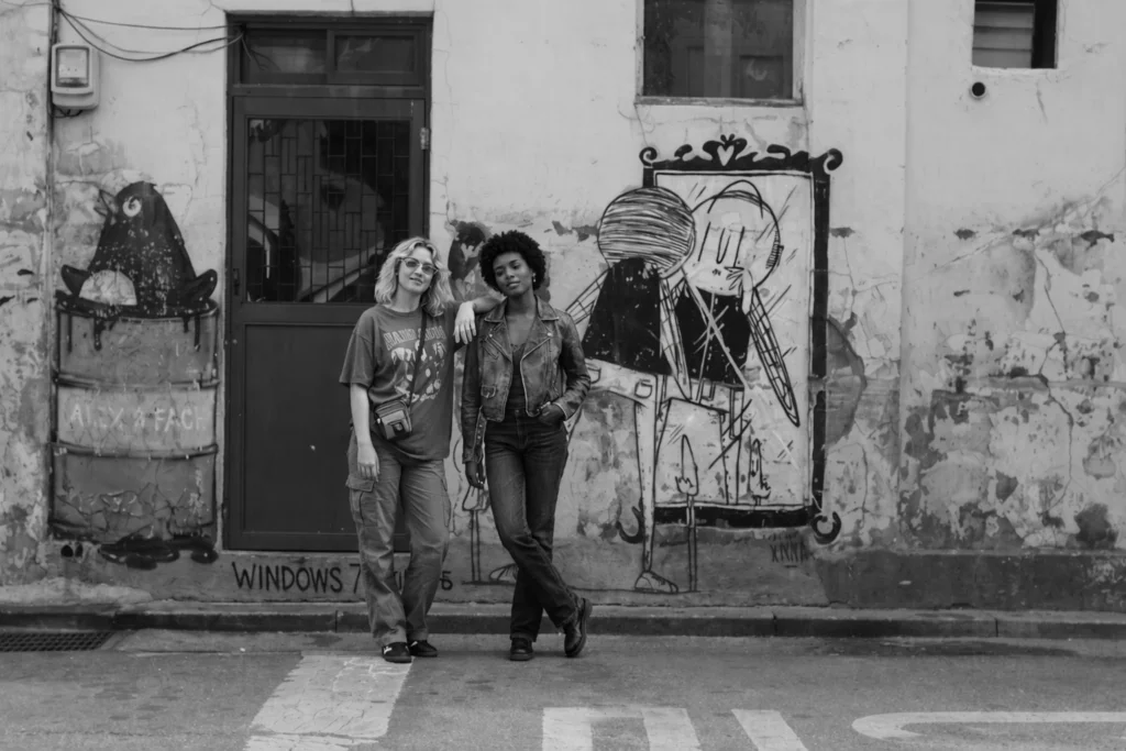 Two foreign women posing for a unique street-style photo in front of a painted industrial wall in Seongsu, Seoul, with urban graffiti and a creative factory district atmosphere.