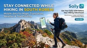 A professional marketing banner showing a female hiker on a scenic rocky mountain ridge in South Korea, checking a map on her smartphone. The banner features the Saily logo and text promoting eSIM services for mobile data needs like navigation, translation, and weather updates while hiking.